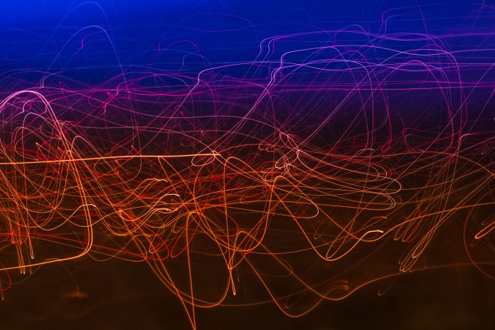 Abstract photo of colorful light trails in blue, pink, and orange twisting across a dark background.