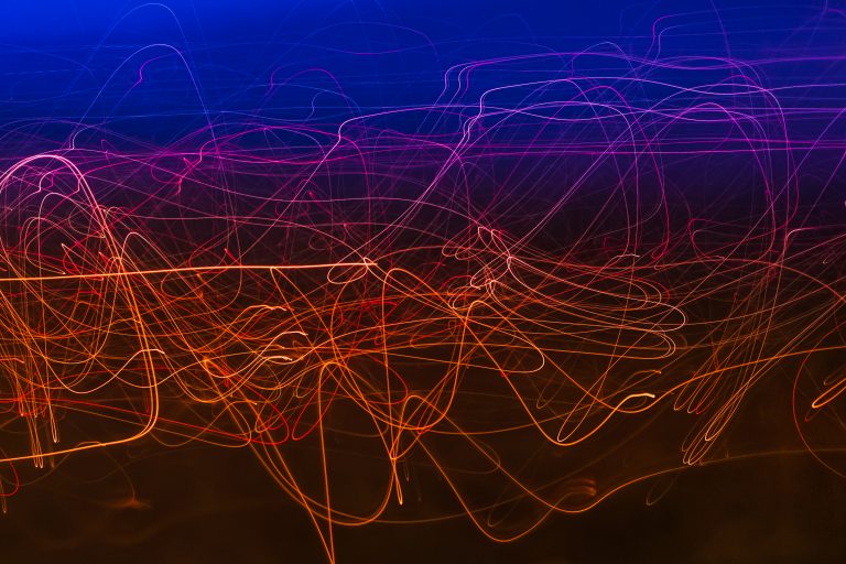 Abstract photo of colorful light trails in blue, pink, and orange twisting across a dark background.