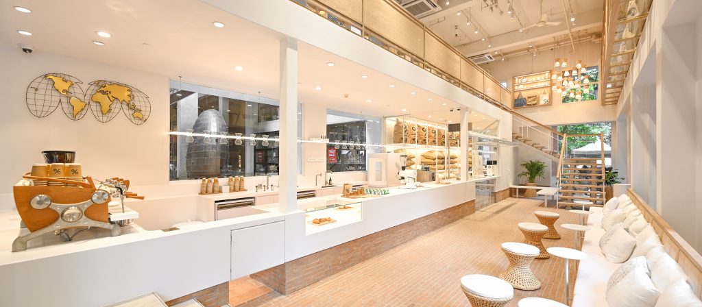 Bright cafe interior with pastry counter, coffee machine, and seating area along a brick base. The open-plan space includes glass display cases and a world-map wall art piece on the left.
