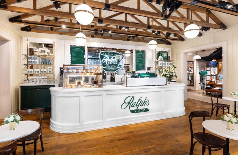 White curved counter with Ralph's Coffee logo, pastry display case, and green menu boards inside a cozy cafe.