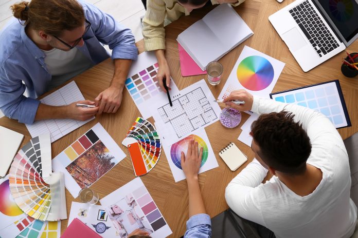 Top-down view of a design team at a wooden table examining color swatches, charts, and a laptop.